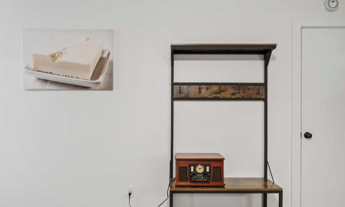 Una habitación con una pared blanca, una estantería de madera con una radio y una puerta.