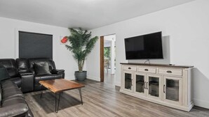 A living room with a sofa, coffee table, TV, cabinet, and a potted plant. - Forest River Farmhouse Retreat (Fall Creek)