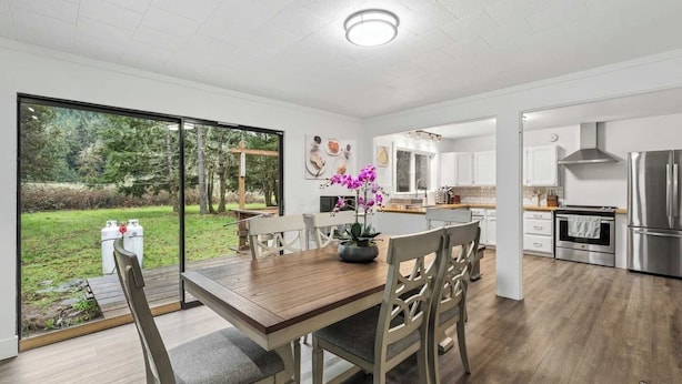 A modern kitchen with white cabinets, a stainless steel refrigerator, and a dining area with a wooden table and chairs. - Forest River Farmhouse Retreat (Fall Creek)