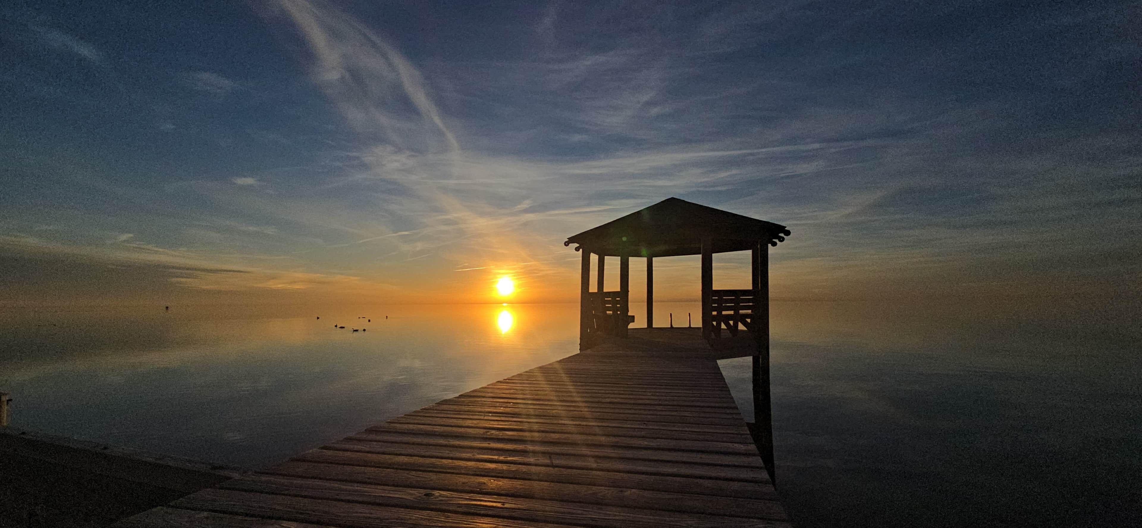 A wooden pier leading to a gazebo with a sunset in the background.