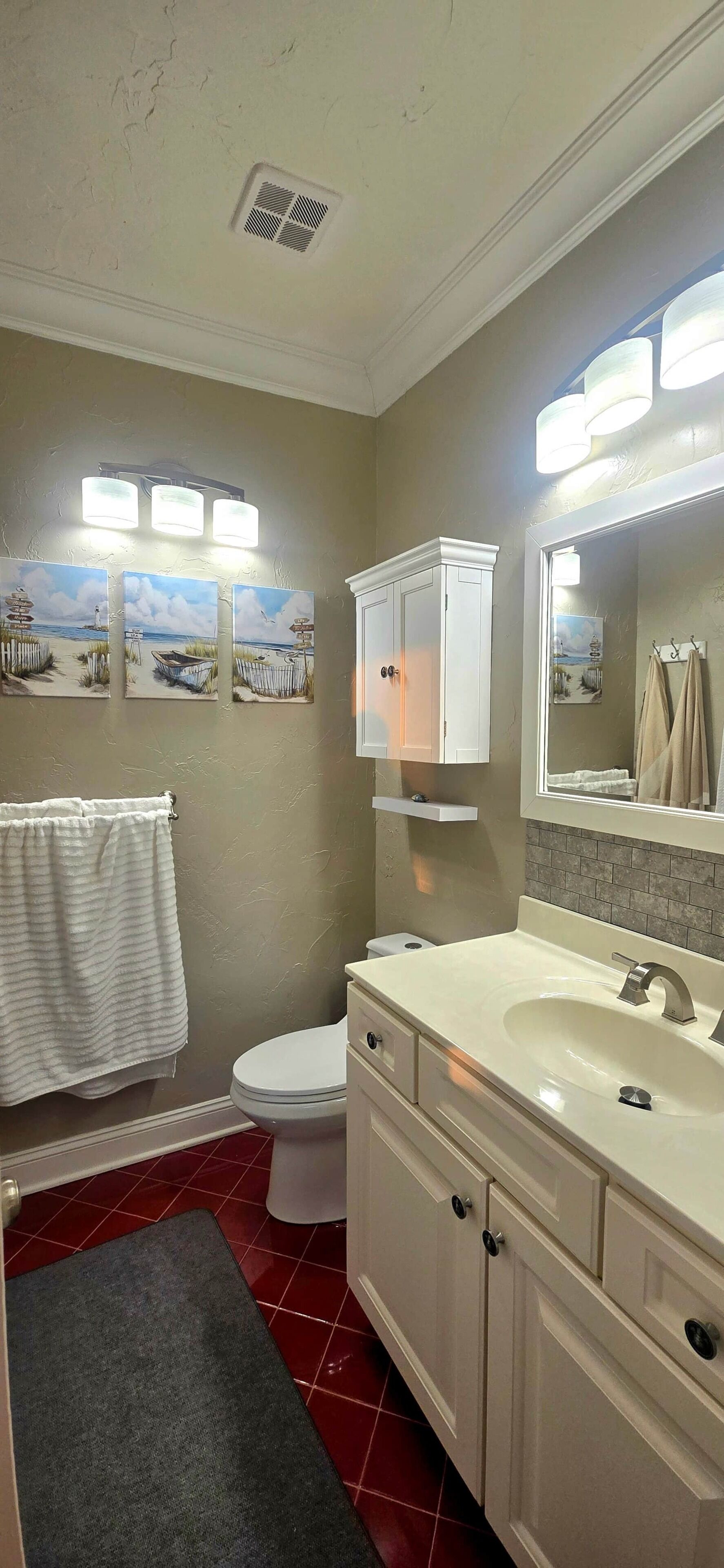A bathroom with a toilet, sink, cabinet, towel rack, and a small rug.