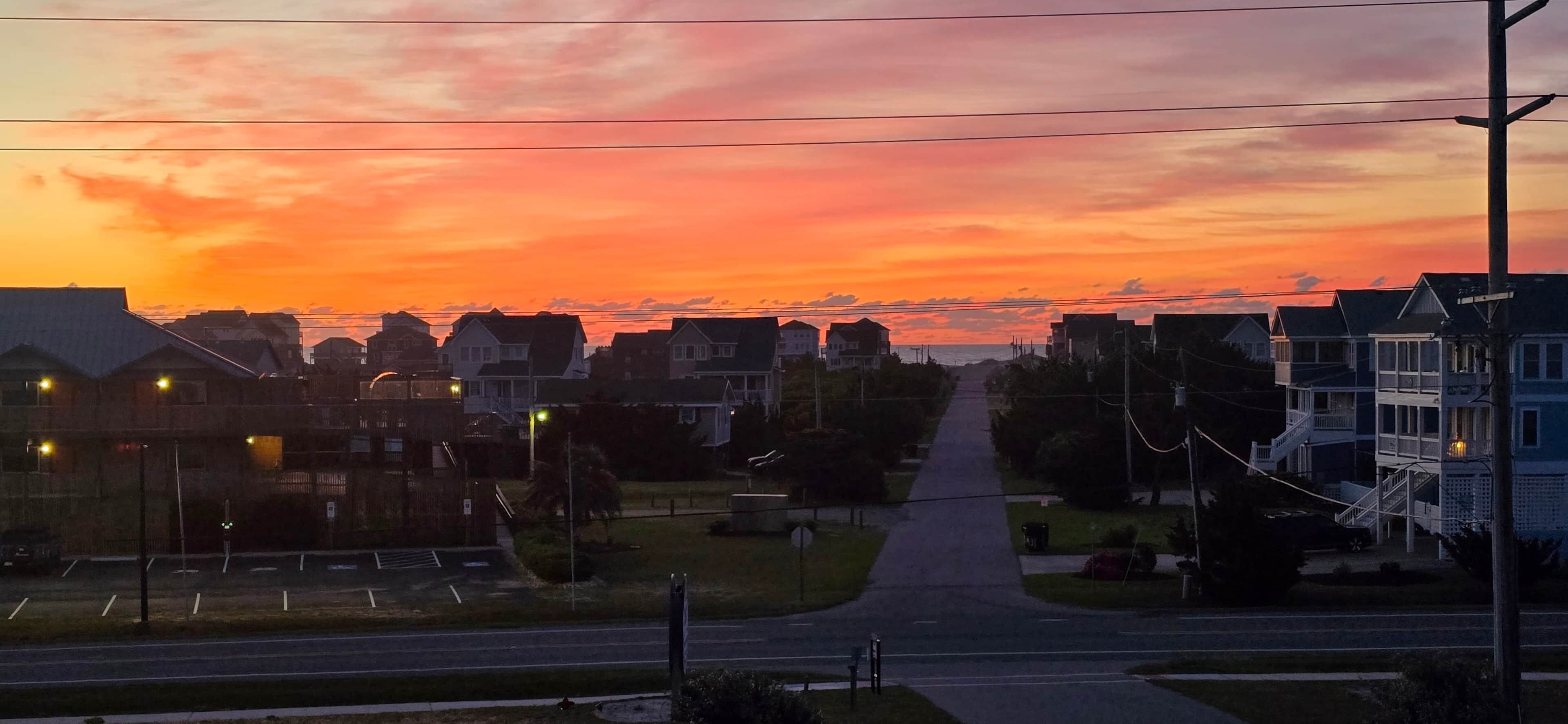 A residential street at sunset with houses, a clear sky, and a visible road.