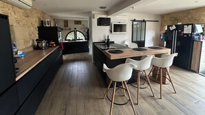 Cozinha moderna com ilha central, banquetas brancas, parede de pedra decorativa e uma janela grande.