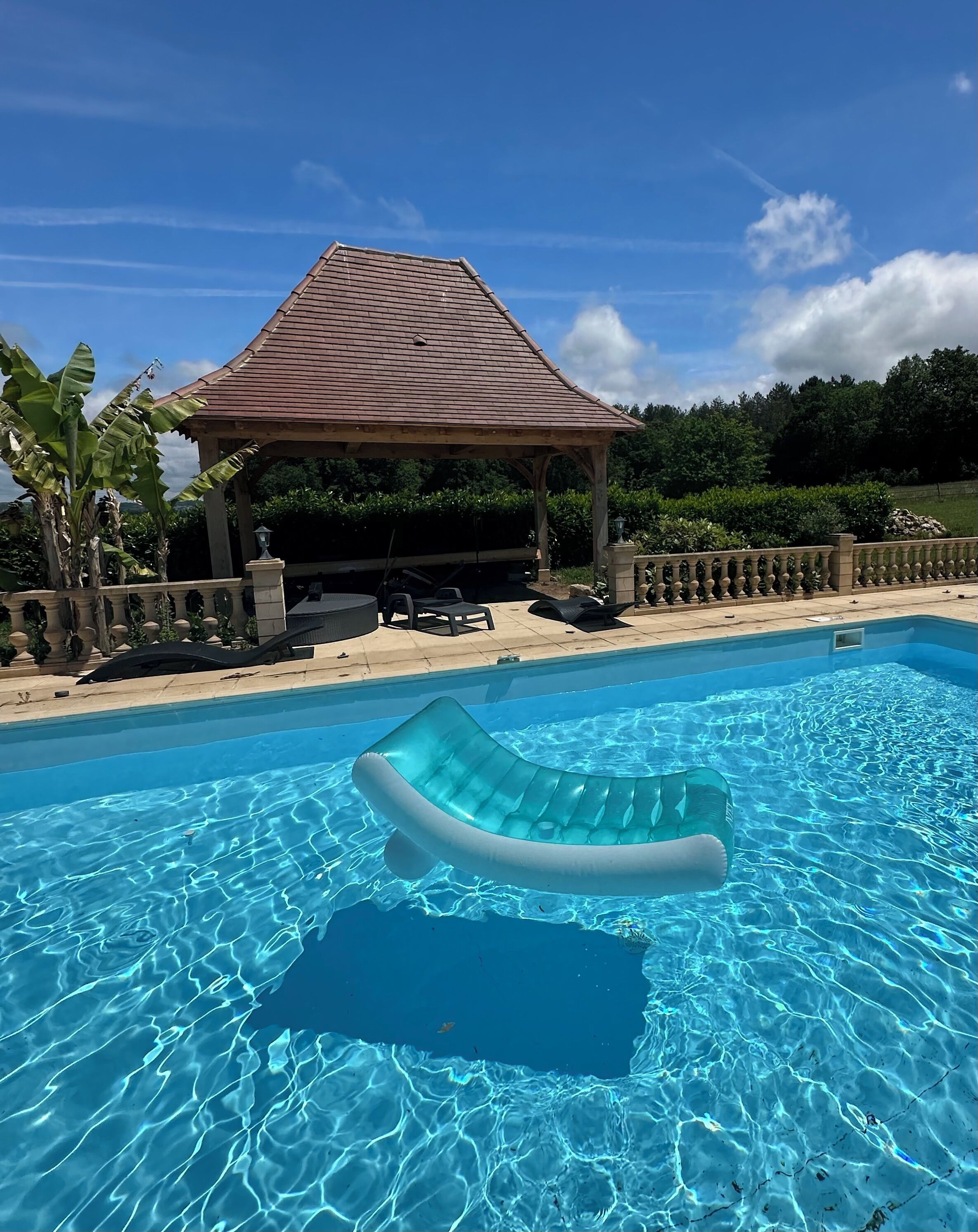 Piscina cristalina con un sillón flotante, un pabellón y una barandilla de piedra.