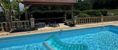 Piscina cristalina con un sillón flotante, un pabellón y una barandilla de piedra.