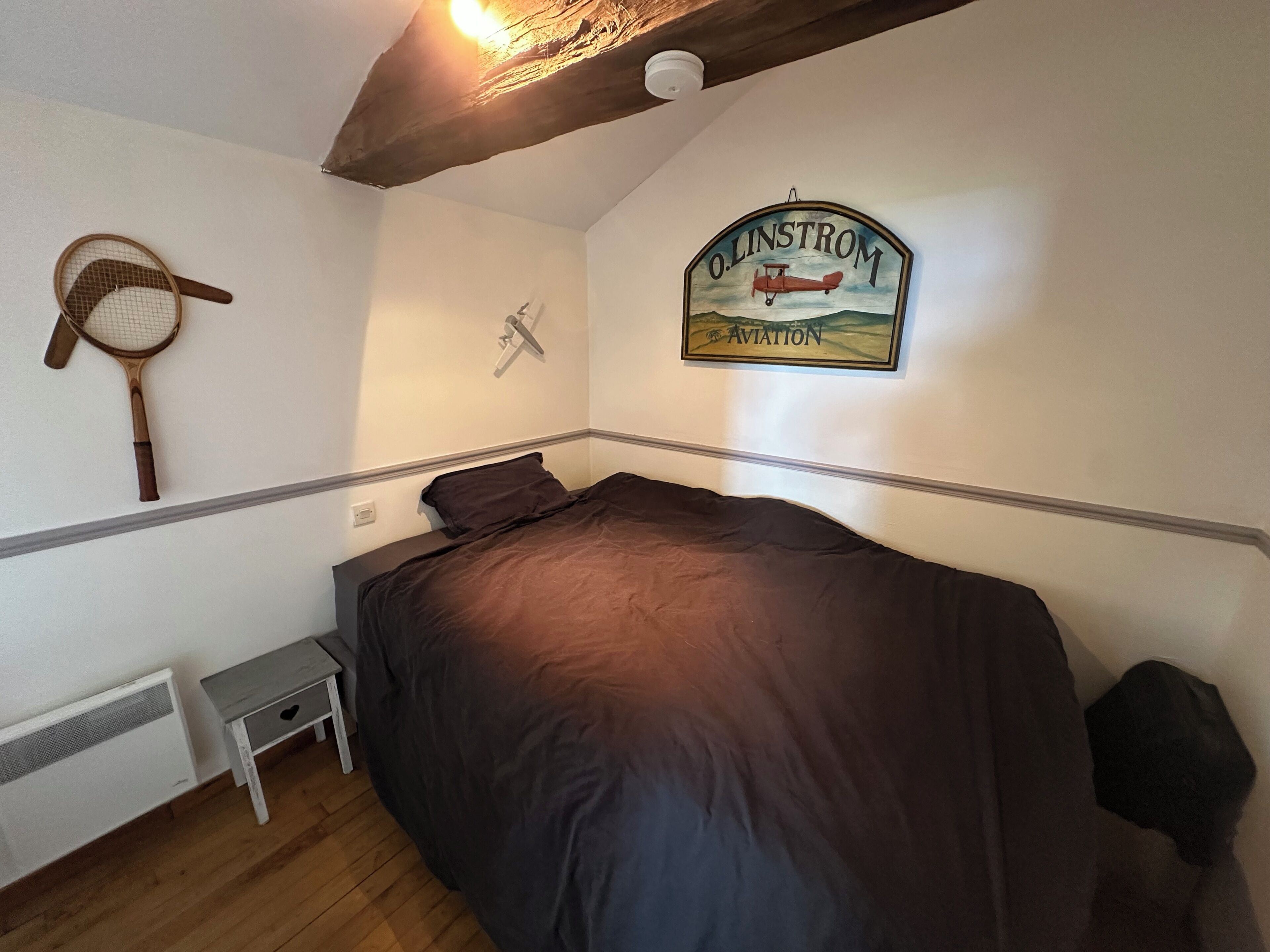 Un dormitorio con cama, una mesita de noche pequeña, un ventilador de pared, una lámpara de pared y una decoración mural.