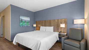 A hotel room with a bed, a chair, a nightstand, and a wall-mounted lamp.