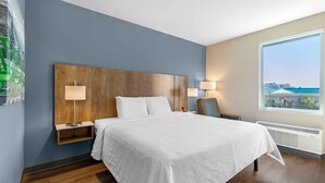 A hotel room with a large bed, bedside lamps, a nightstand, a chair, a window with a view, and a wall-mounted artwork. - Extended Stay America Premier Suites - Denver International Airport (Denver)