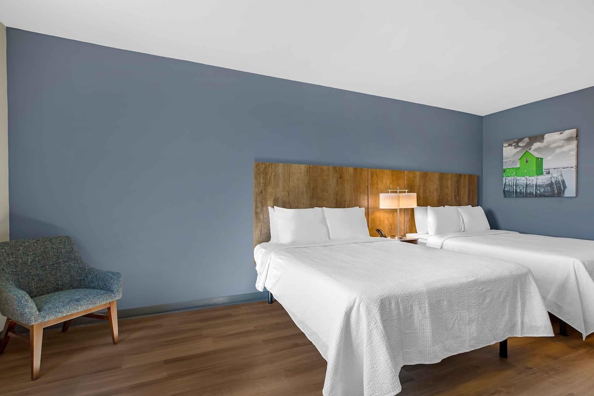 A hotel room with two beds, a wooden headboard, a chair, and a painting on the wall.