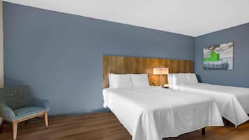 A hotel room with two beds, a wooden headboard, a chair, and a painting on the wall.
