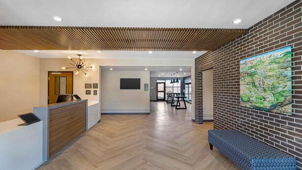 A reception area with a wooden reception desk, a bench, a map on the wall, and a herringbone-patterned floor. - Extended Stay America Premier Suites - Denver International Airport (Denver)