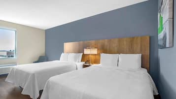 A hotel room with two beds, a wooden headboard, a nightstand, a lamp, and a window with a city view.