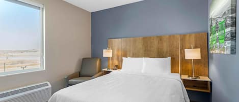 A hotel room with a large bed, two bedside tables with lamps, a chair, a window with a view, and a wall-mounted artwork.