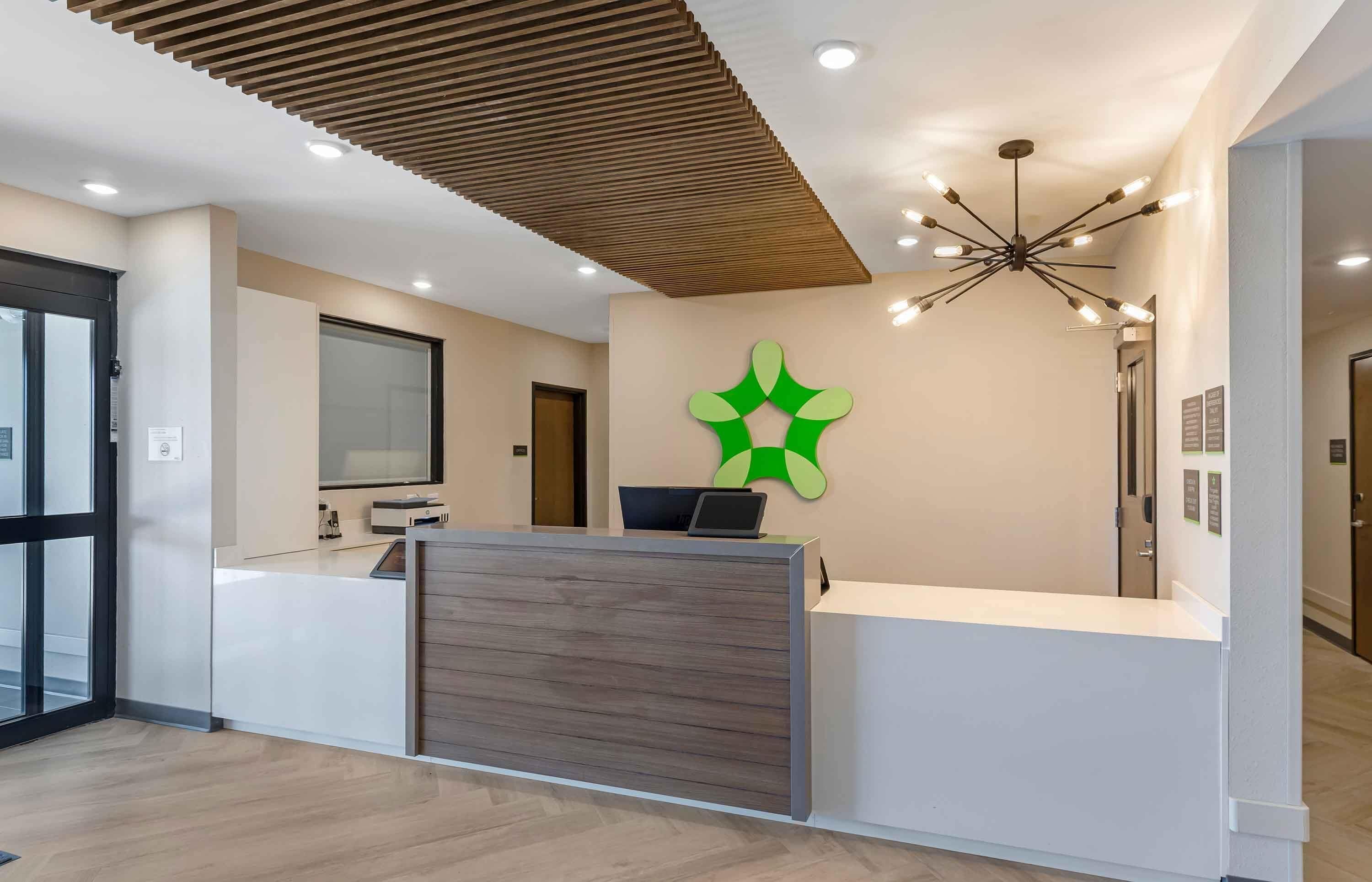 Een modern ogend receptiebalie, een groen logo aan de muur en een plafond met een uniek lamparmatuur.