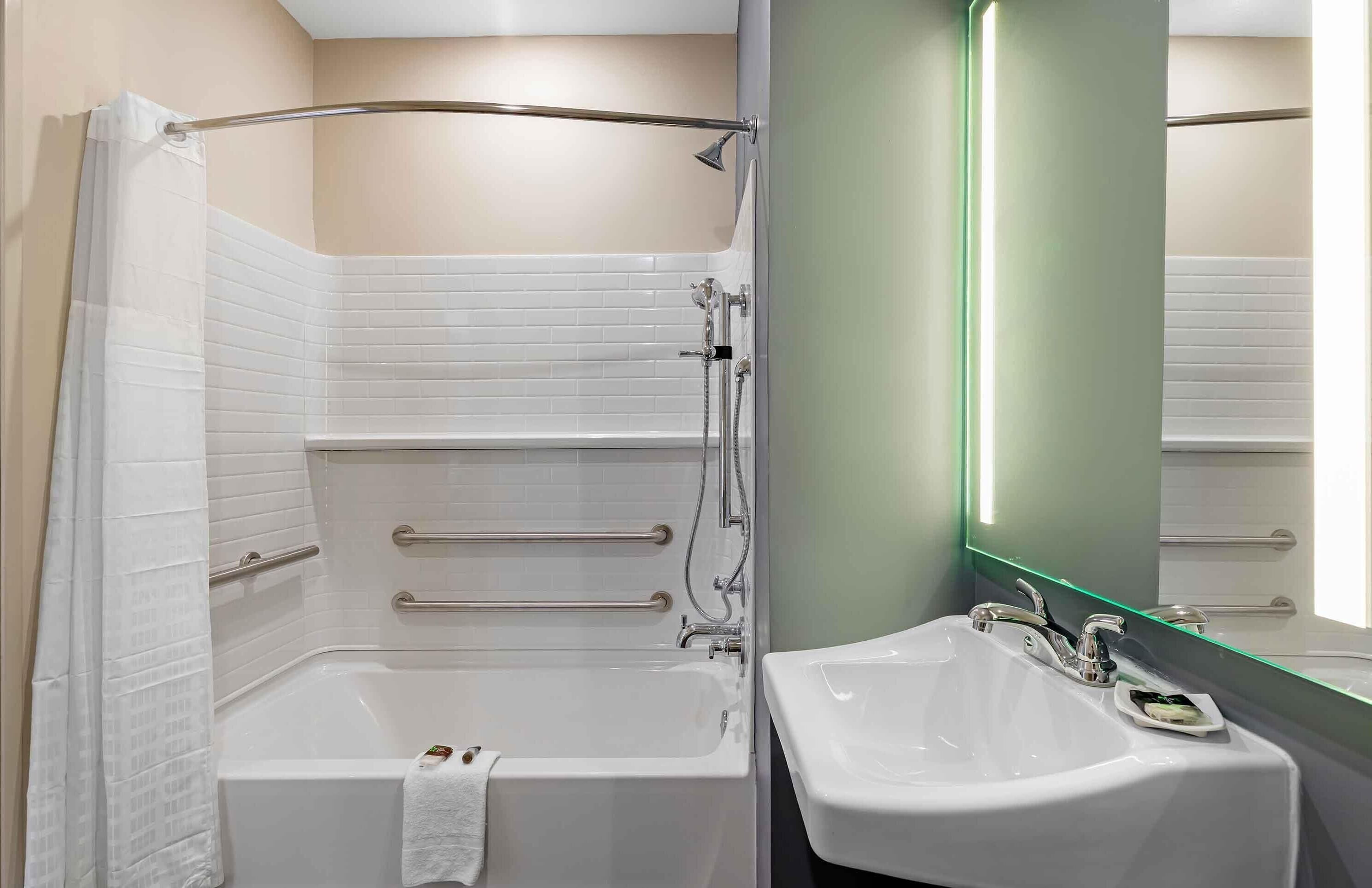 Un baño moderno con ducha a ras de suelo, bañera, lavabo y espejo con luz verde.