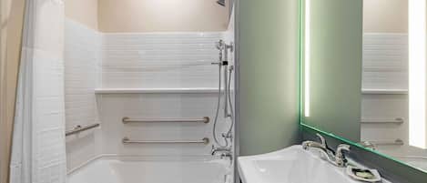 A modern bathroom with a walk-in shower, a bathtub, a sink, and a mirror with a green light.