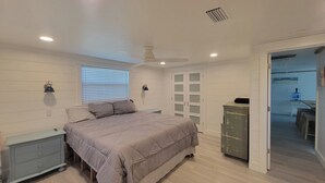 Quarto com cama, mesas de cabeceira, guarda-roupa, ventoinha no teto e janela com persianas.