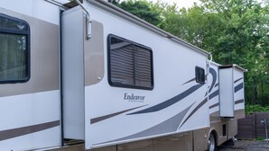 Un veicolo ricreativo con porta scorrevole, una finestra con tende e un logo con la scritta 'Endeavor by Holiday Rambler'.