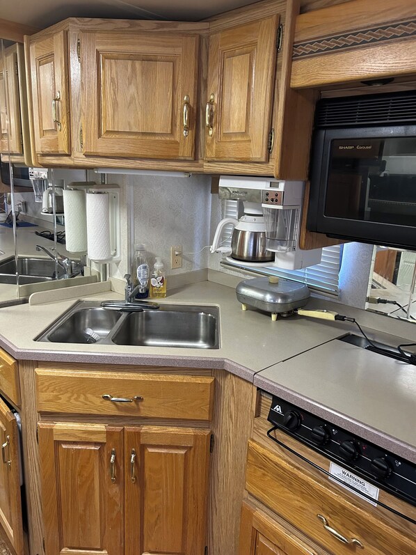 A kitchen with wooden cabinets, a stainless steel sink, a coffee maker, and a microwave.
