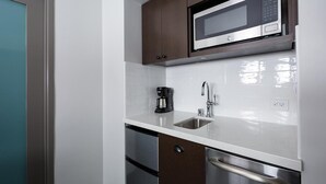 A compact kitchen with a microwave, coffee maker, stainless steel sink, and a dishwasher.