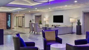 A hotel lobby with seating areas, a reception desk, a flat-screen TV, and a sign indicating elevators to parking and a street.