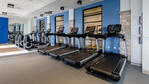 A gym with multiple treadmills lined up against a blue wall, a brick accent wall, and a large window.