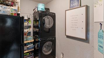 Een wasruimte met gestapelde wasmachines en drogers, een koelkast, en planken met diverse spullen.