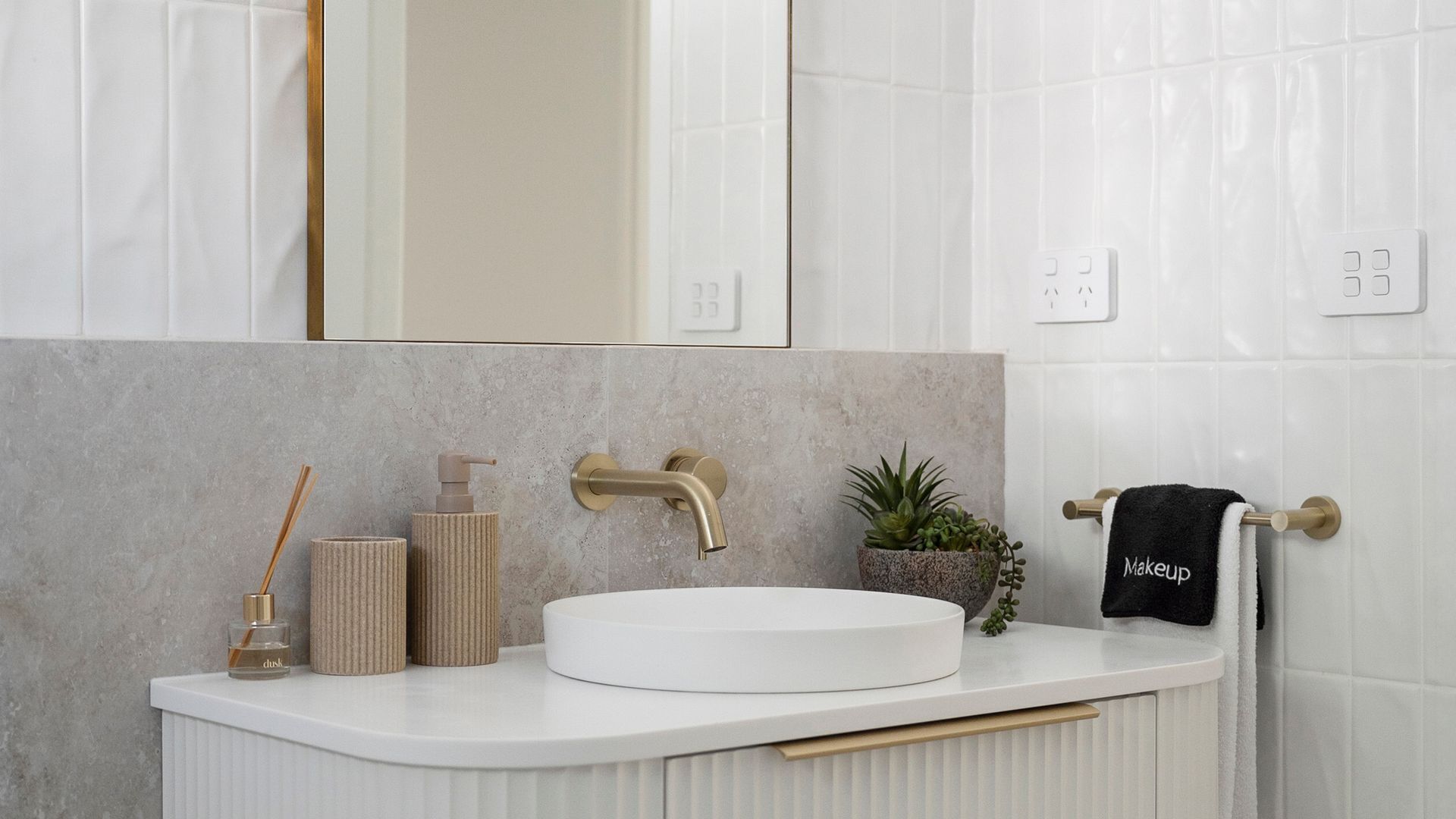 Ein Badezimmer mit einem weißen Waschbecken, einem goldenen Wasserhahn, einem Spiegel und einem Handtuchhalter mit einem Handtuch.