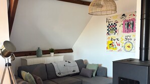 A cozy living room with a sofa, a wooden coffee table, a floor lamp, a wall art piece, and a black wood-burning stove.