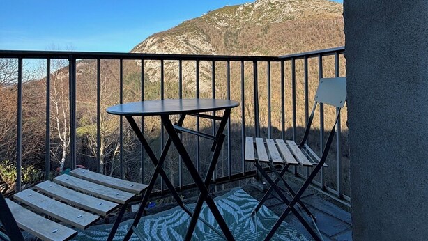 A balcony with a table and chairs, a view of a mountain, and a railing.