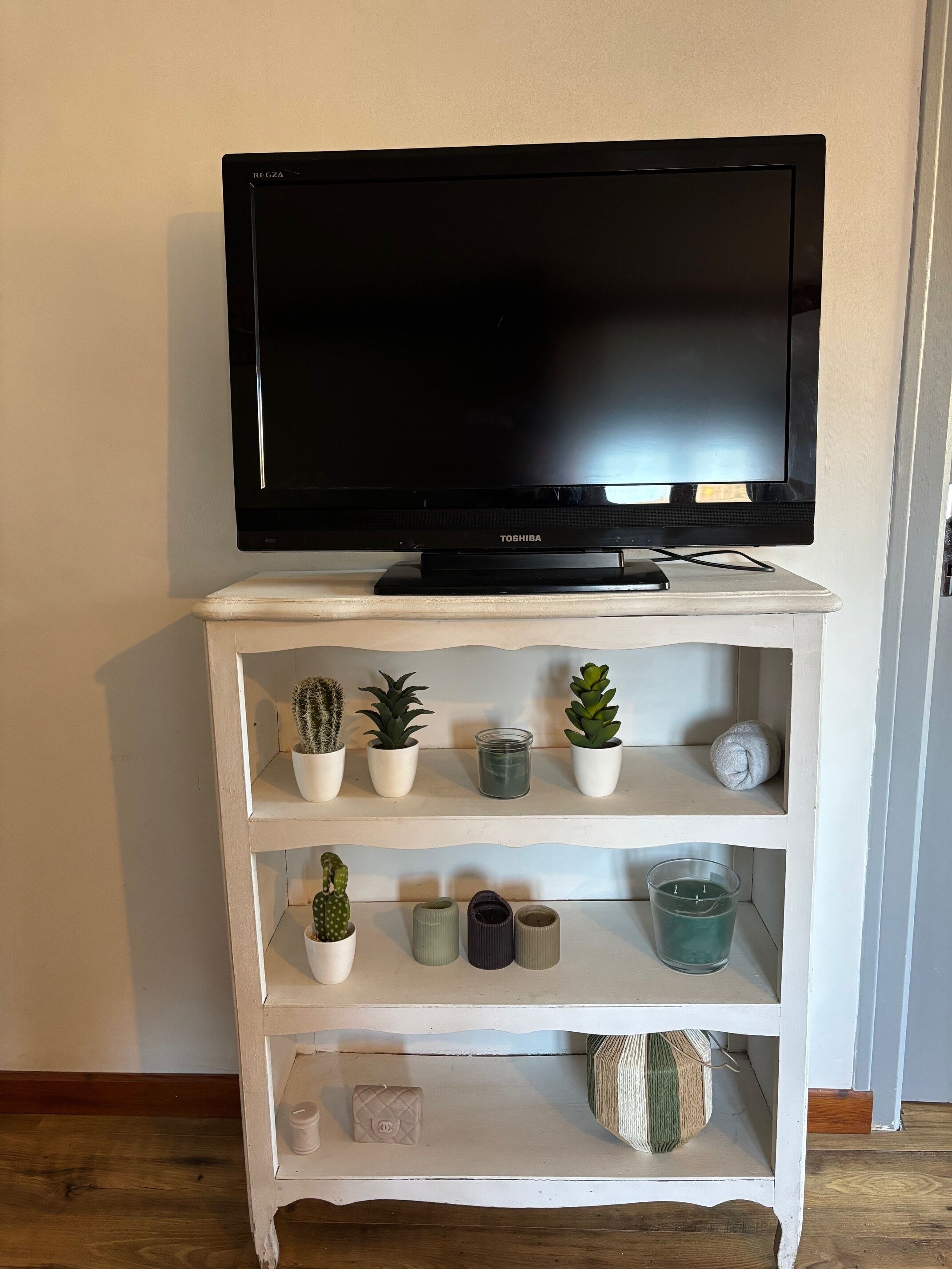 Ett vitt TV-bord med en platt-TV ovanpå, hyllor med krukväxter, ljus och dekorativa föremål.