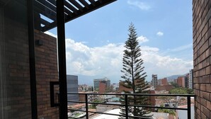 A balcony with a view of a cityscape, including buildings and a tree. - Affordable accommodation with terrace in Medellín - LOF (Medellín)