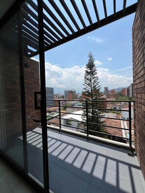 A balcony with a view of a cityscape, including buildings and a tree. - Affordable accommodation with terrace in Medellín - LOF (Medellín)