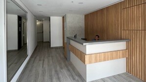 A reception area with a wooden reception desk, a 'BIENVENIDO' mat, and a hallway with a wooden floor. - Affordable accommodation with terrace in Medellín - LOF (Medellín)