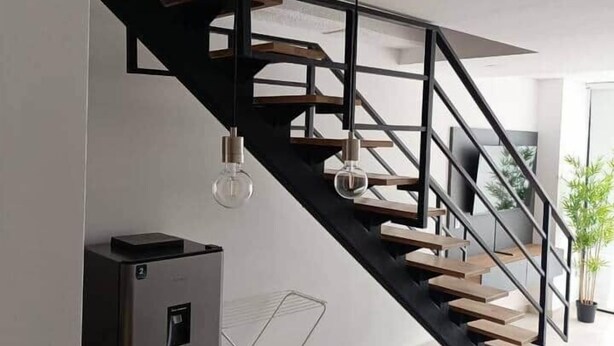 A modern staircase with a minimalist design, a black metal railing, and pendant lighting. - Affordable accommodation with terrace in Medellín - LOF (Medellín)
