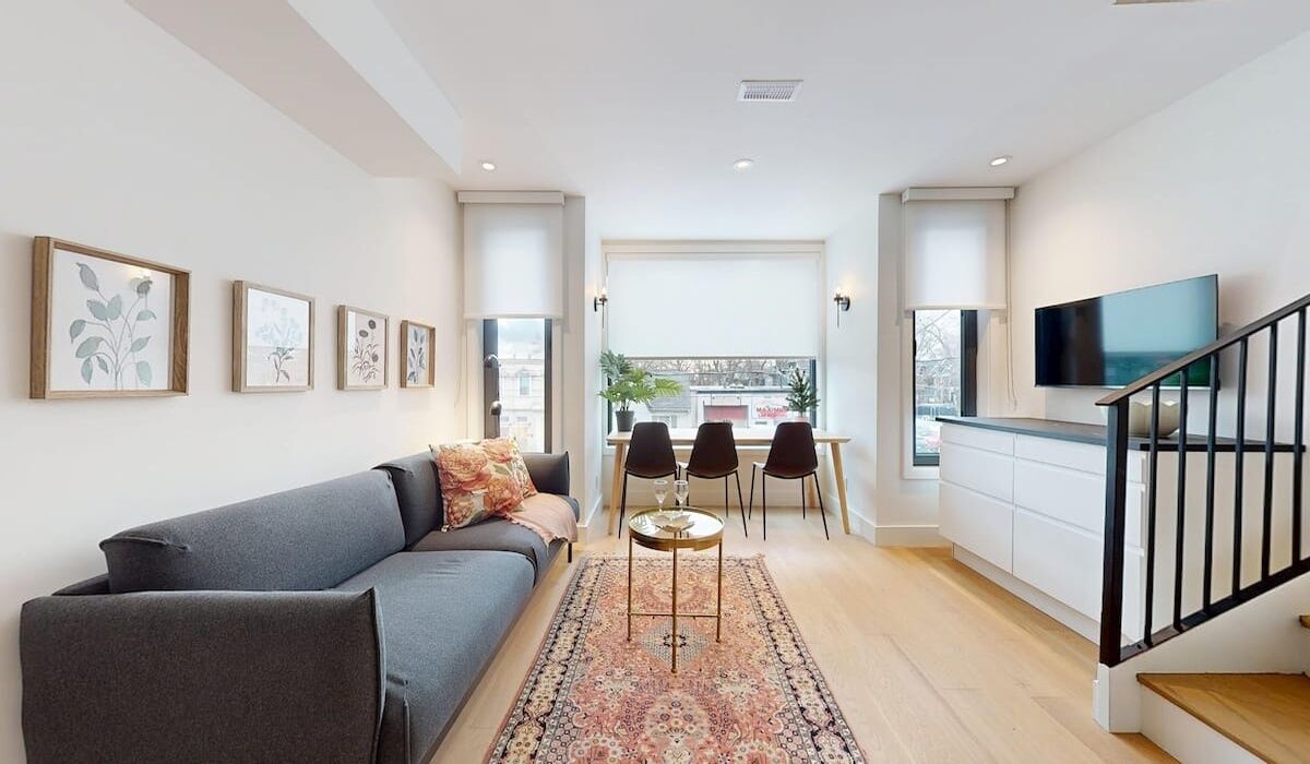 Ein modernes Wohnzimmer mit einer Couch, einem Essbereich mit Stühlen, einem Fernseher und gerahmten Kunstwerken an den Wänden.