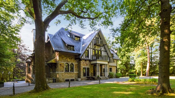 A historic building with a steeply pitched roof, large windows, and a prominent entrance with a porch. - Lovely home in Spa with sauna (Spa)