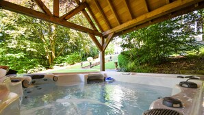 A hot tub area with a wooden pergola overhead, surrounded by lush greenery. - Lovely home in Spa with sauna (Spa)