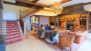A spacious living room with a fireplace, a staircase with a red carpet, and a bookshelf filled with books. - Lovely home in Spa with sauna (Spa)