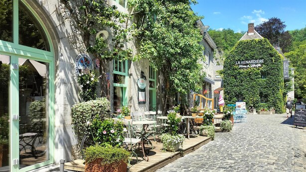 Una calle adoquinada con mesas al aire libre, un edificio con un letrero que dice 'LA RENARDIE' y un ventanal grande a la izquierda.