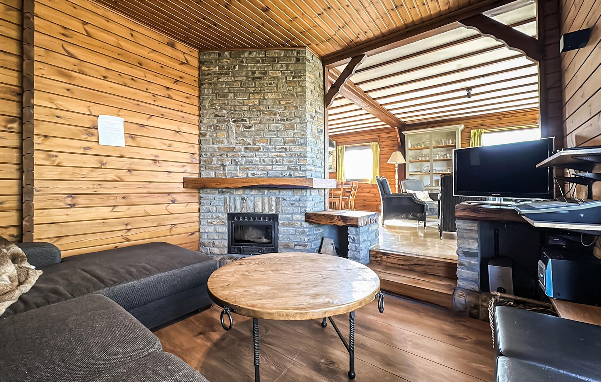 A cozy cabin interior with a stone fireplace, wooden walls, a sofa, a round table, and a television.