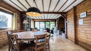 Un interior de madera con una mesa redonda y sillas, una lámpara colgante y vistas a través de un ventanal.