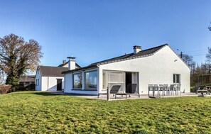A modern house with a large glass door, a patio with chairs, and a well-maintained lawn.
