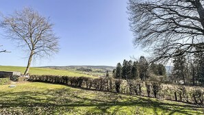 Un paysage rural caractérisé par un ciel dégagé, un chemin bordé d’arbres et des collines lointaines.