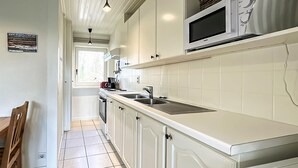 A kitchen with white cabinets, a sink, a microwave, and a window.