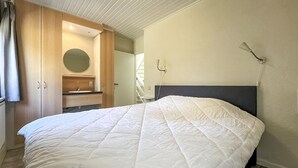Ein Schlafzimmer mit einem Bett, einem Holzschrank, einem runden Spiegel, einem Waschbecken und einer Wandleuchte.