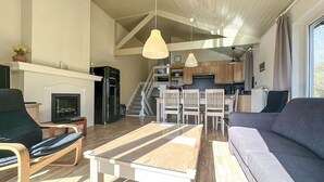 Ein modernes Wohnzimmer mit einer Couch, einem Esstisch und Stühlen, einer Küche im Hintergrund sowie einer Treppe, die in eine obere Ebene führt.