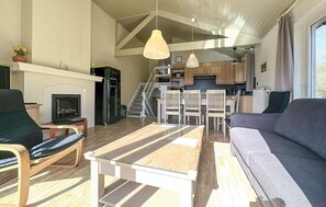 Ein modernes Wohnzimmer mit einer Couch, einem Esstisch und Stühlen, einer Küche im Hintergrund sowie einer Treppe, die in eine obere Ebene führt.