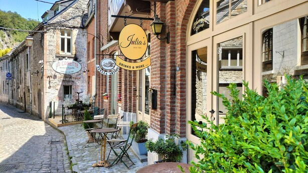 Eine Kopfsteinpflasterstraße mit Außenbestuhlung vor einem Café namens 'Julia's Juice Bar'.