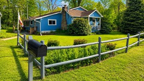 A blue house with a porch, surrounded by a wooden fence and lush greenery.